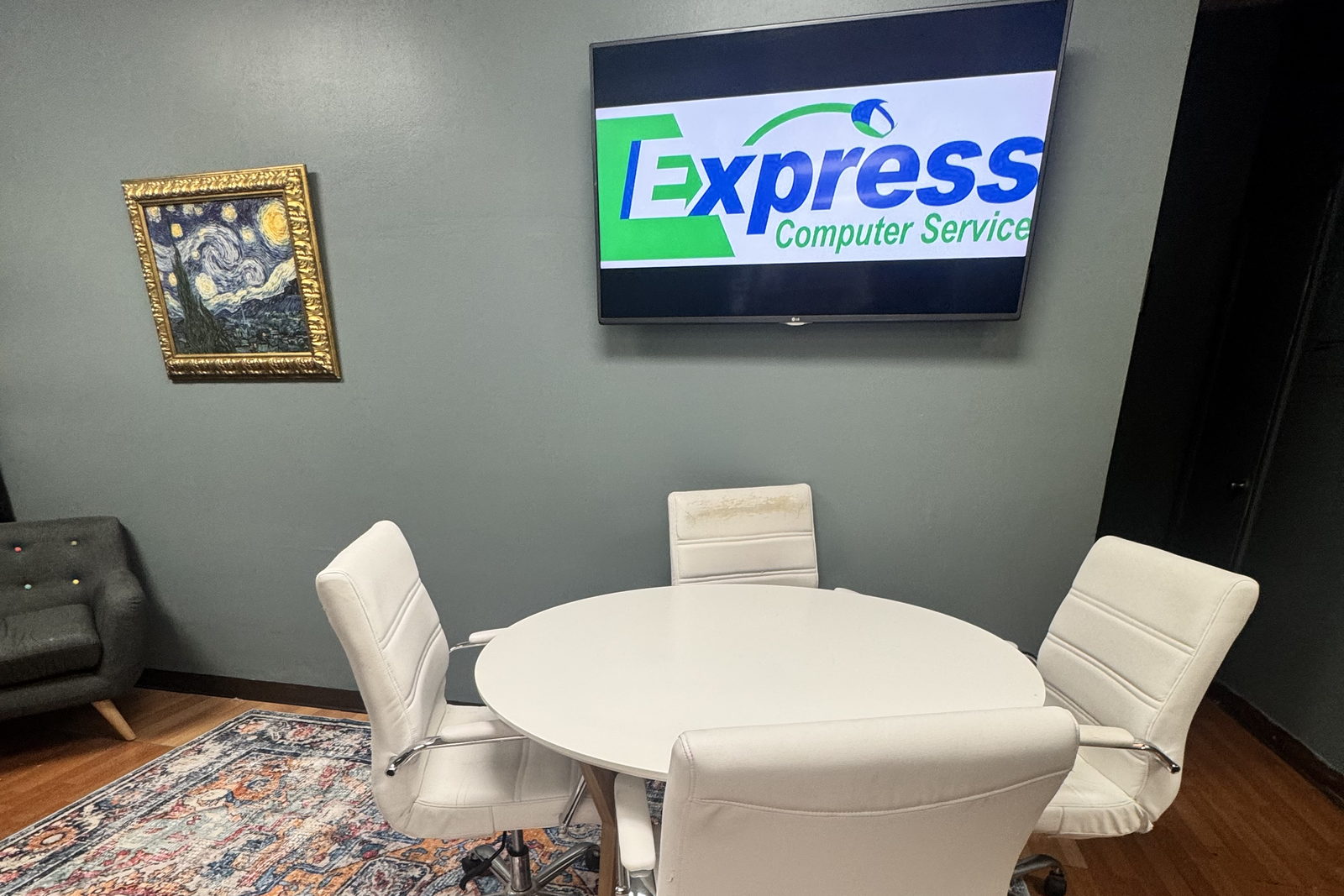 The Express IT Solutions meeting room in Fayetteville, New York: a round white table with four chairs, a wall mounted screen showing the company logo, and a framed print on the wall.