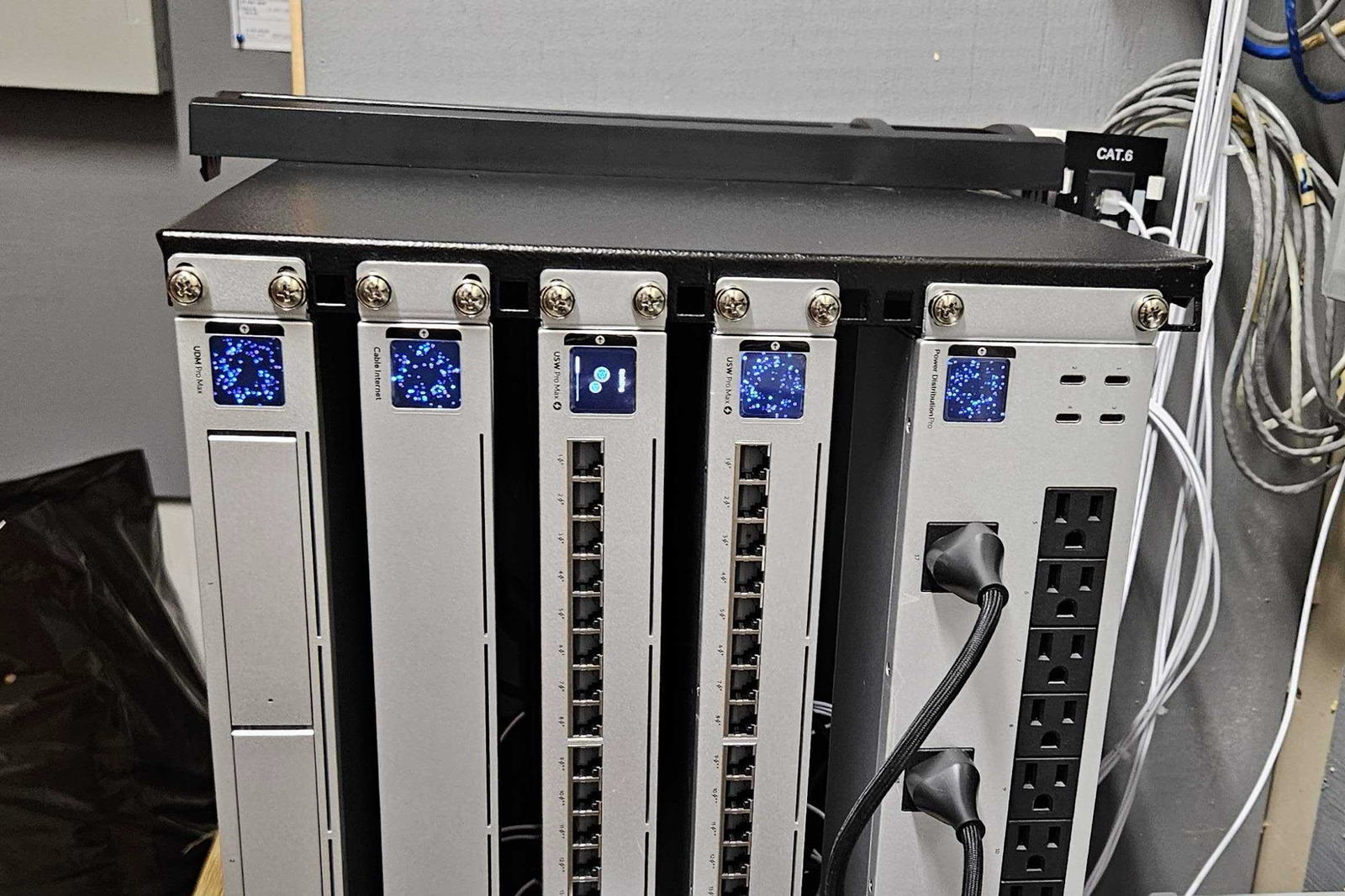 Close view of an installed network rack: a gateway, two PoE switches and a rack power distribution unit, with patch cables run and the cable run labelled Cat 6.