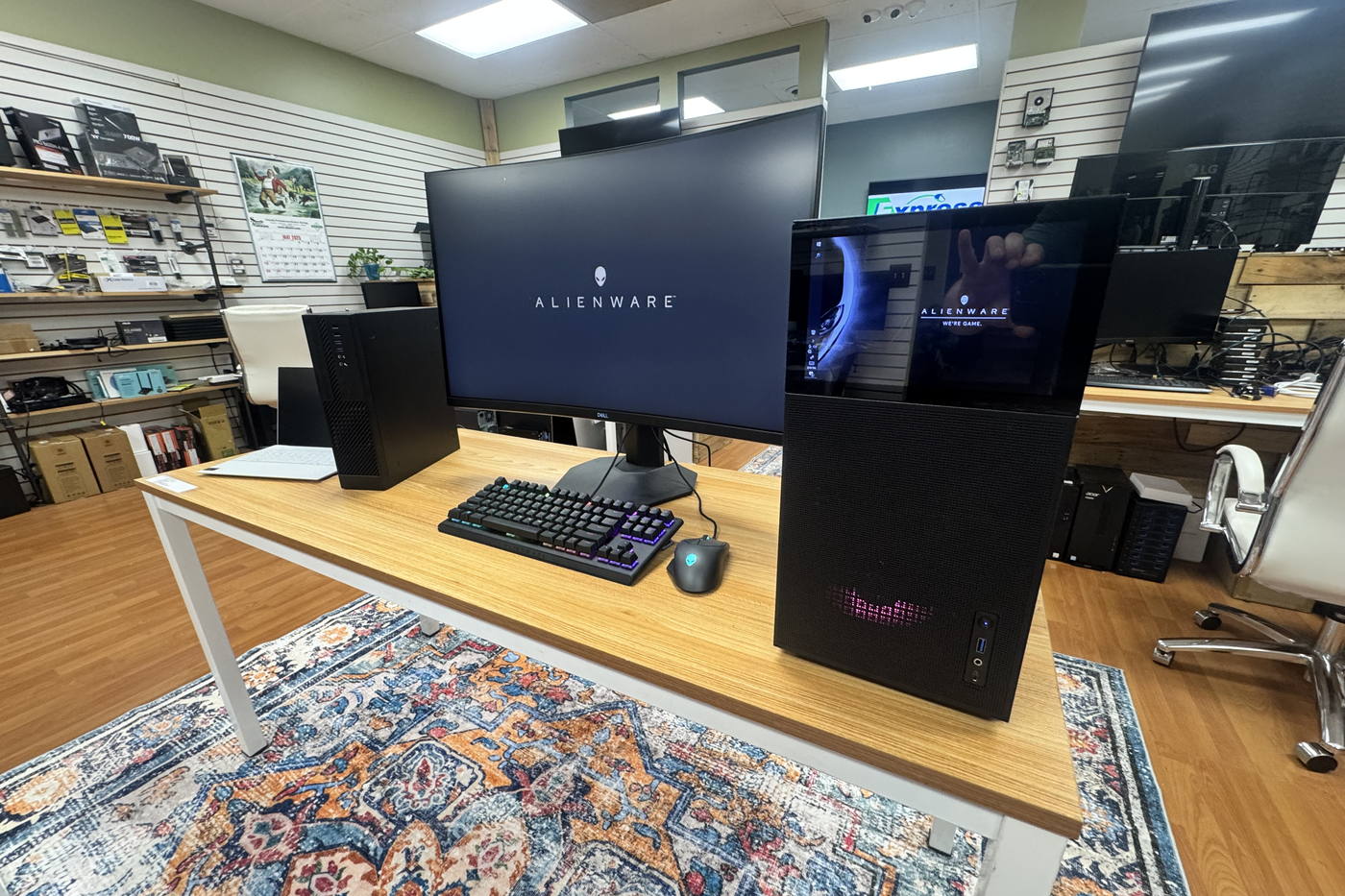 A workstation on display in the Express IT store: a monitor, a mechanical keyboard and two desktop towers, with components and accessories on the wall behind.