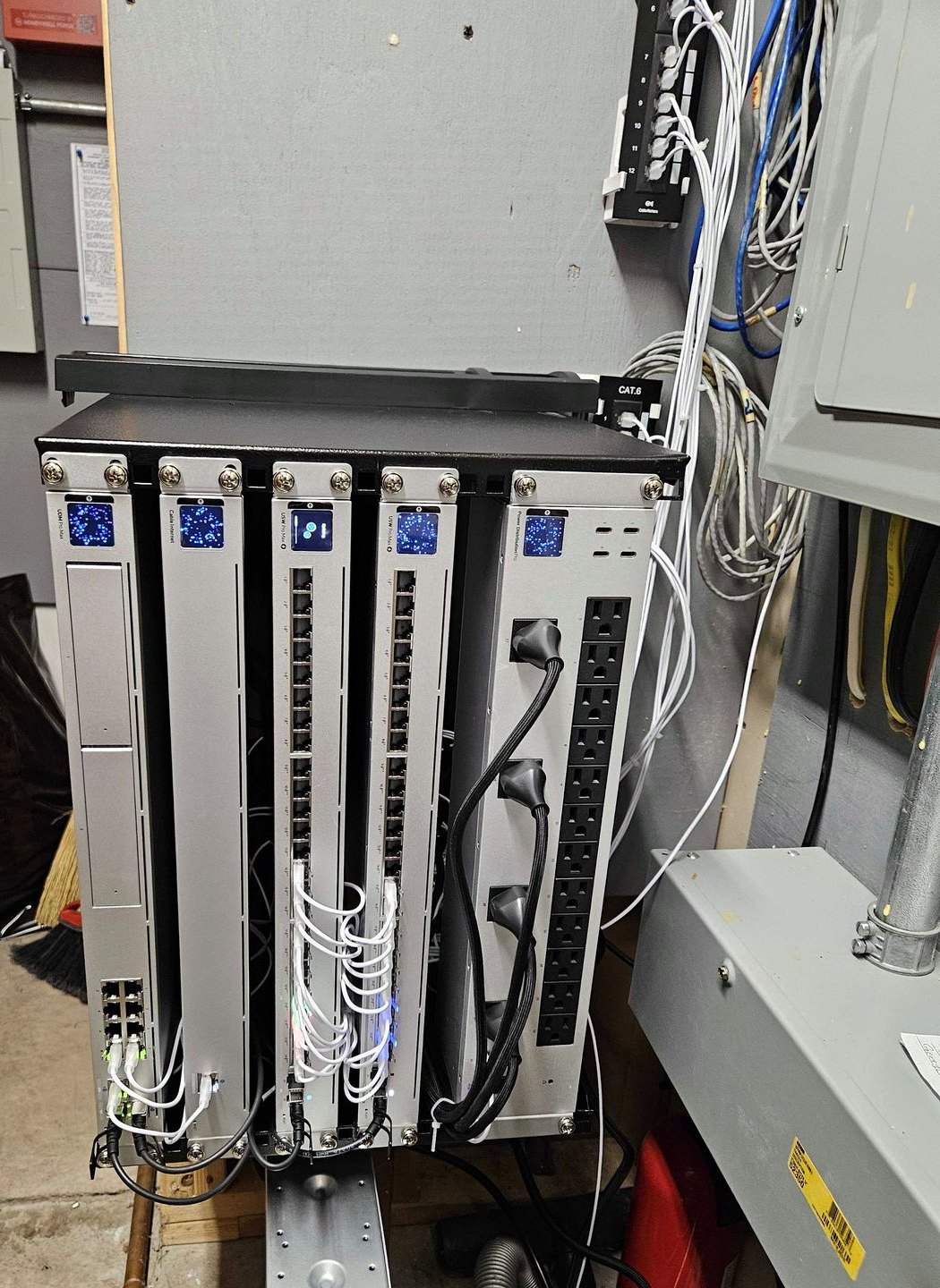A completed network cabinet in a mechanical room: a wall mounted rack holding a switch and patch panels, every run terminated and dressed into the panel in ordered bundles, with a power distribution strip down the right hand side and the structured cabling carried up into the ceiling.