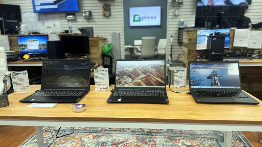 Business laptops set out on a display counter in the Express IT showroom, with screens on the wall behind.