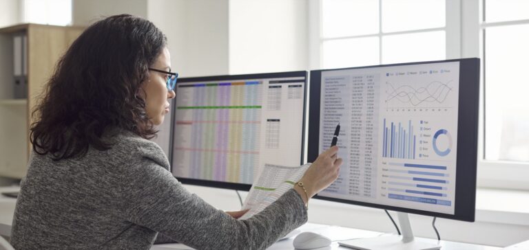 Accountant reviewing spreadsheets on two monitors