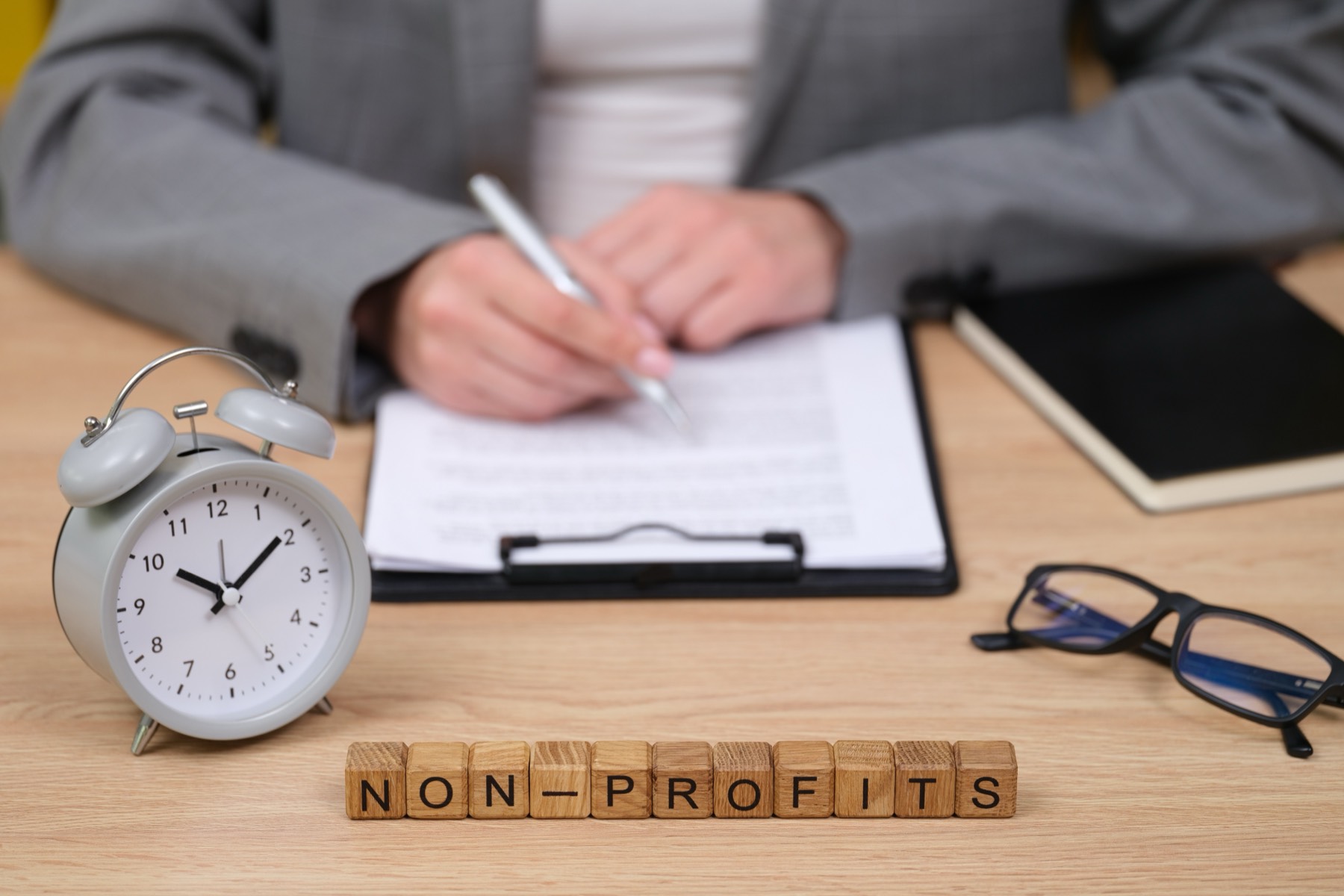 Person signing paperwork at a desk beside wooden blocks that spell non-profits